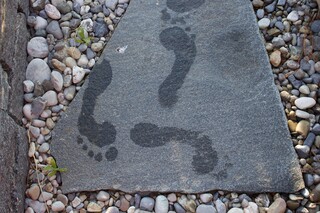 nasse Barfussabdrücke auf Naturstein-Trittplatte im Kiesweg